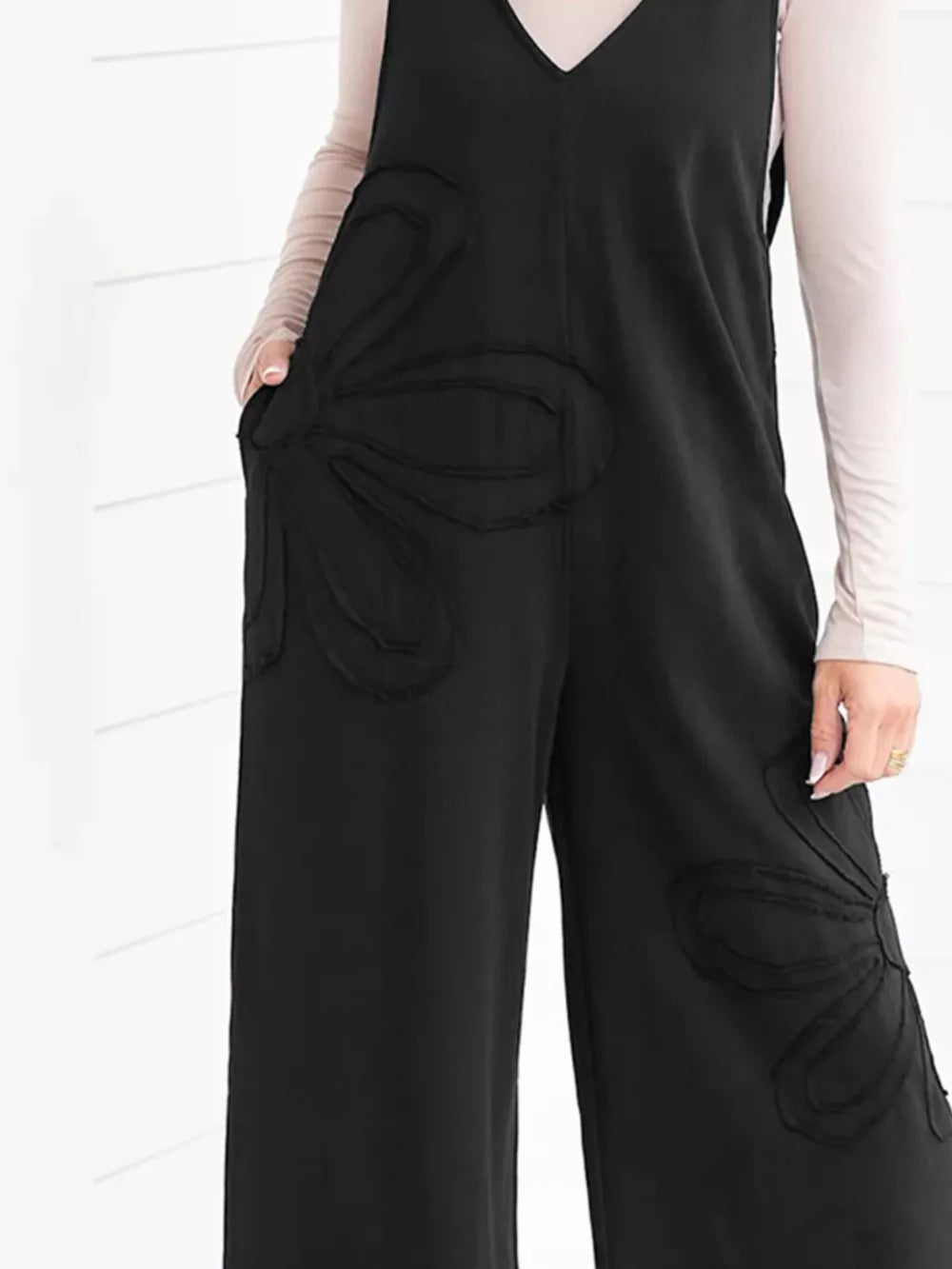 Black cotton maternity romper with wide legs and floral appliqué details.
