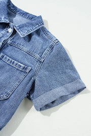 Medium wash denim romper with short sleeves, button-down front, chest pockets, and cuffed hem.