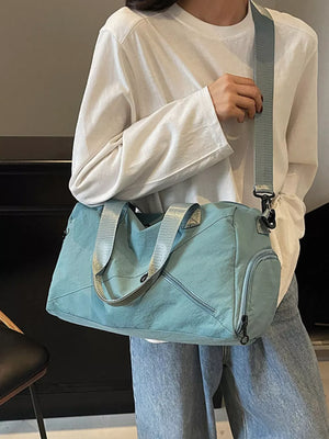 Teal duffel bag with zippered pockets and adjustable shoulder strap, worn by a woman.