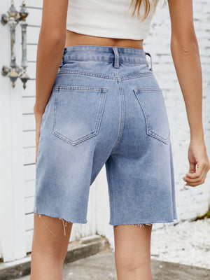 Longline denim cutoff shorts in medium wash with raw hem detail.