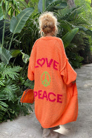Orange knit maxi cardigan with pink LOVE and green PEACE peace sign graphic on back.