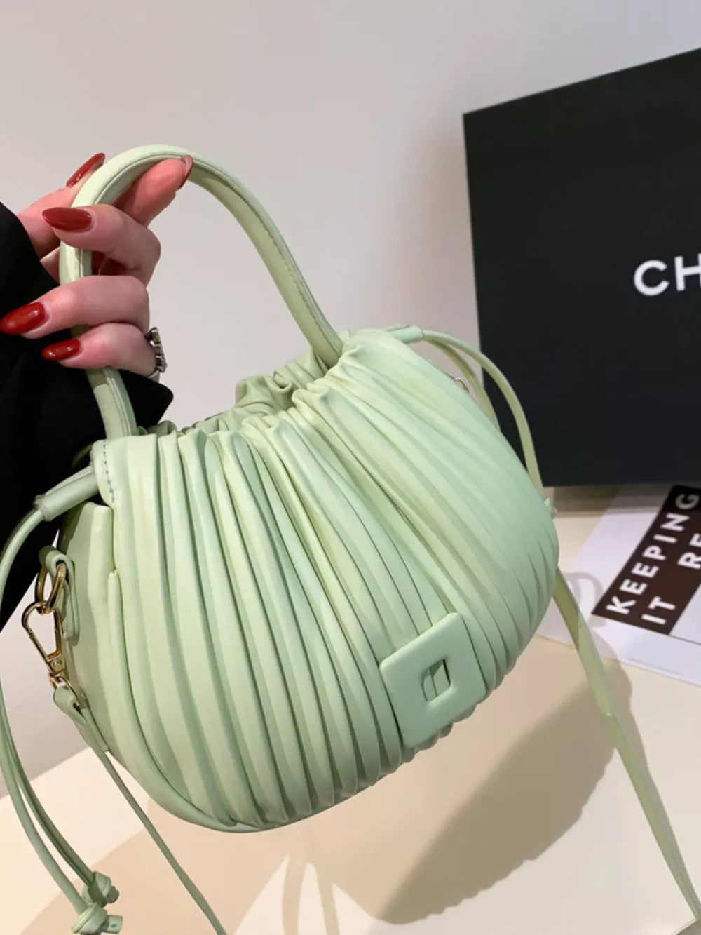 Light green pleated bucket bag with drawstring closure and square detail.