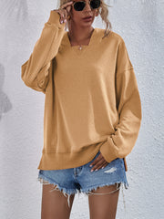 Tan boxy hooded sweatshirt with split hem and V-neck detail.
