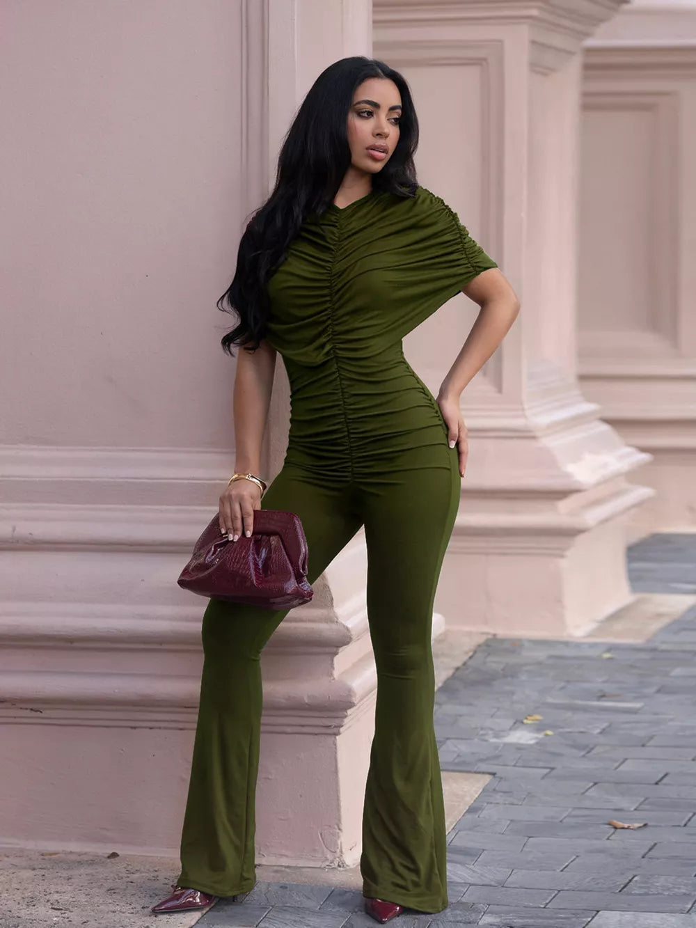 Olive green ruched romper with cap sleeves and flared legs, styled with a burgundy clutch.