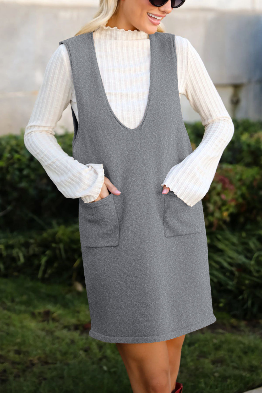 Sleeveless gray knit dress with V-neck and front pockets, layered over a cream ribbed top.