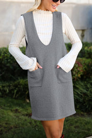 Sleeveless gray knit dress with V-neck and front pockets, layered over a cream ribbed top.