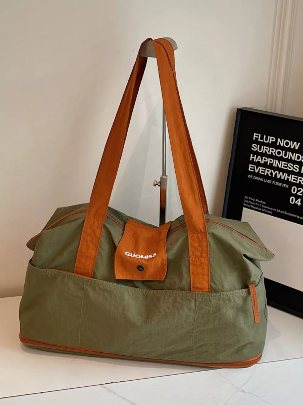 Green nylon travel bag with orange trim and handles, featuring exterior pockets and a small flap pocket with logo.