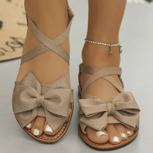 Khaki crisscross bow sandals with ankle straps and a flat sole.