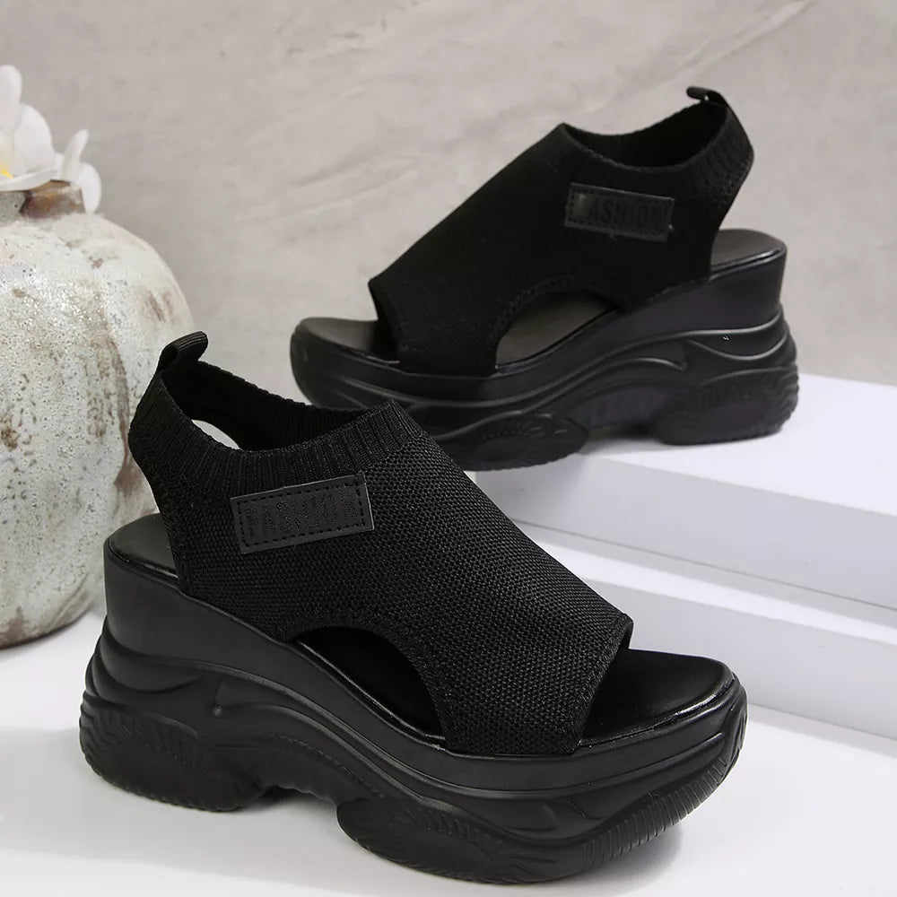Black open-toe wedge sandals with chunky sole and ankle strap.