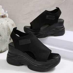 Black open-toe wedge sandals with chunky sole and ankle strap.