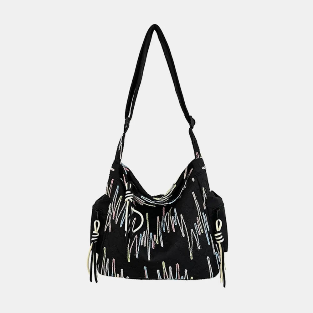 Black slouchy shoulder bag with colorful embroidered abstract pattern and tassel detail.