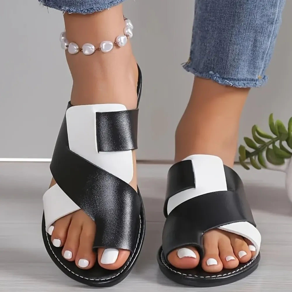 Two-tone black and white crossover toe-loop sandals with a flat sole.