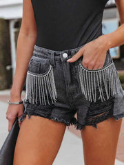 Black distressed denim shorts with crystal fringe detail and raw hem.