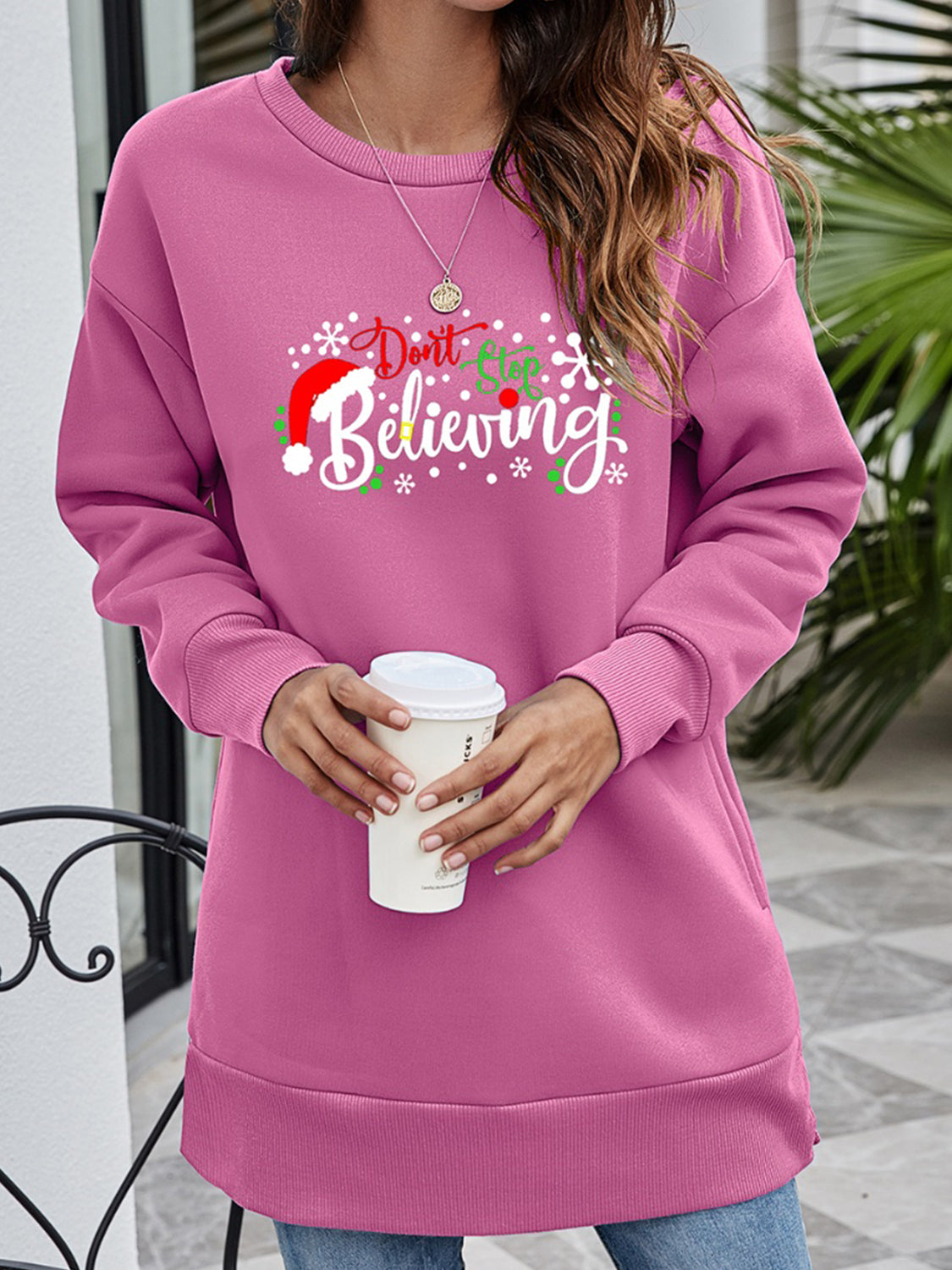 Pink graphic tunic sweatshirt with "Don't Stop Believing" holiday print and Santa hat detail.