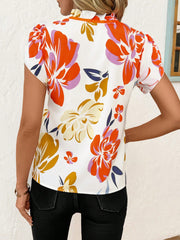 Frilled tie-neck maternity blouse with a vibrant floral print and short sleeves.