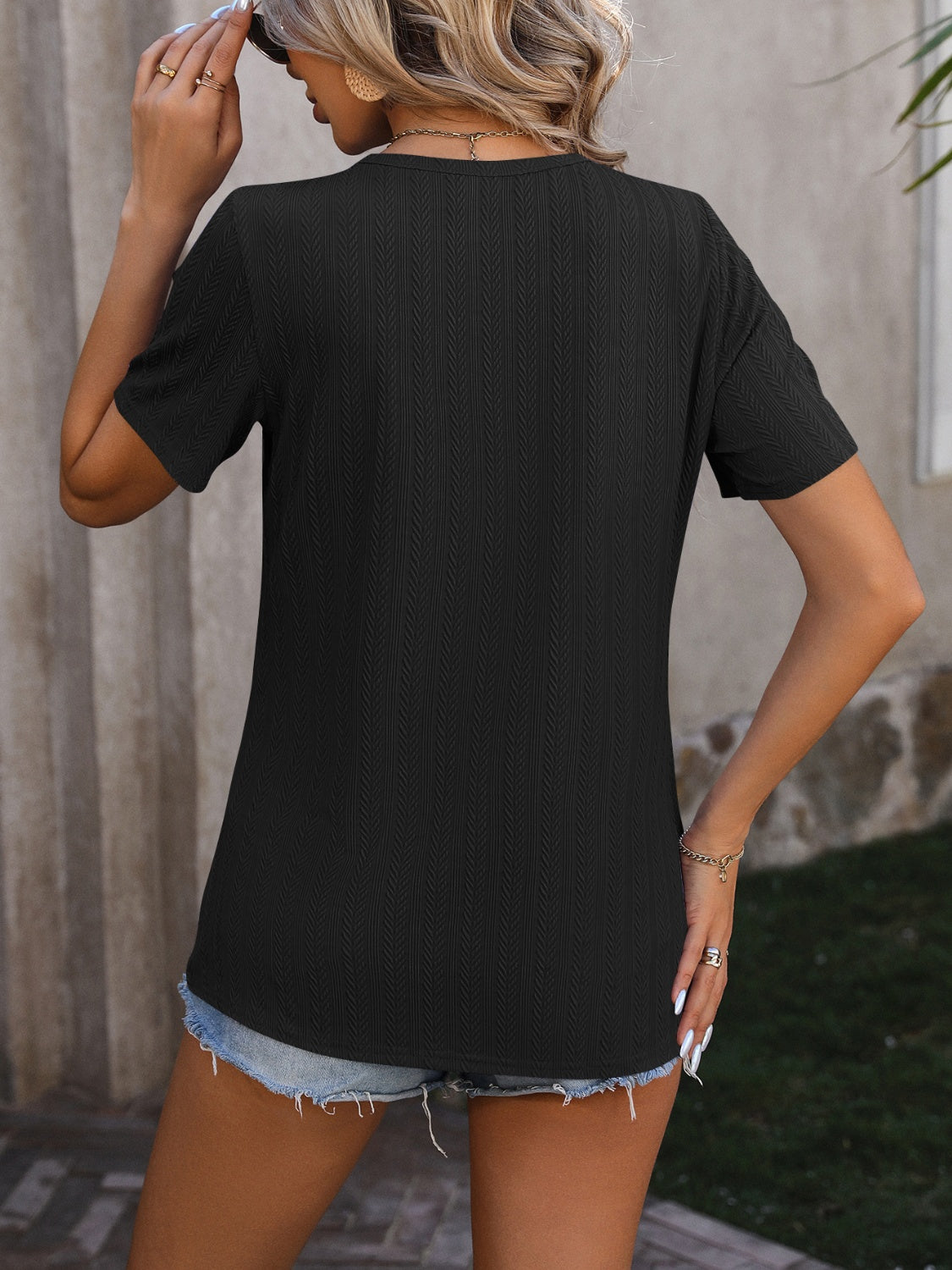 Black textured tee with short sleeves and a split hem, styled with denim shorts.