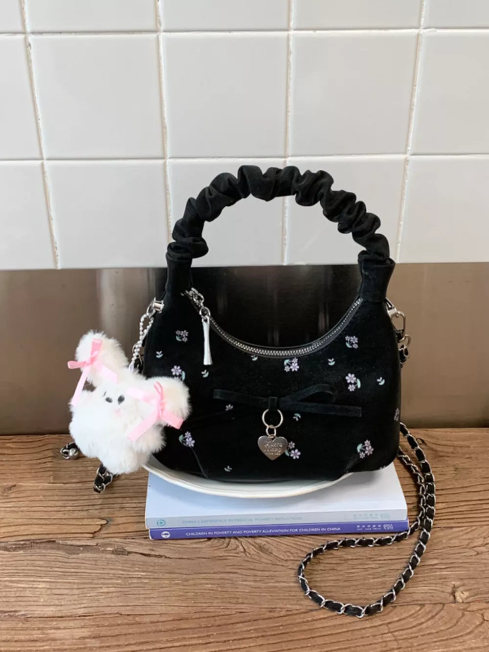 Black ruched crossbody bag with floral embroidery, bow charm, and fluffy bunny charm.