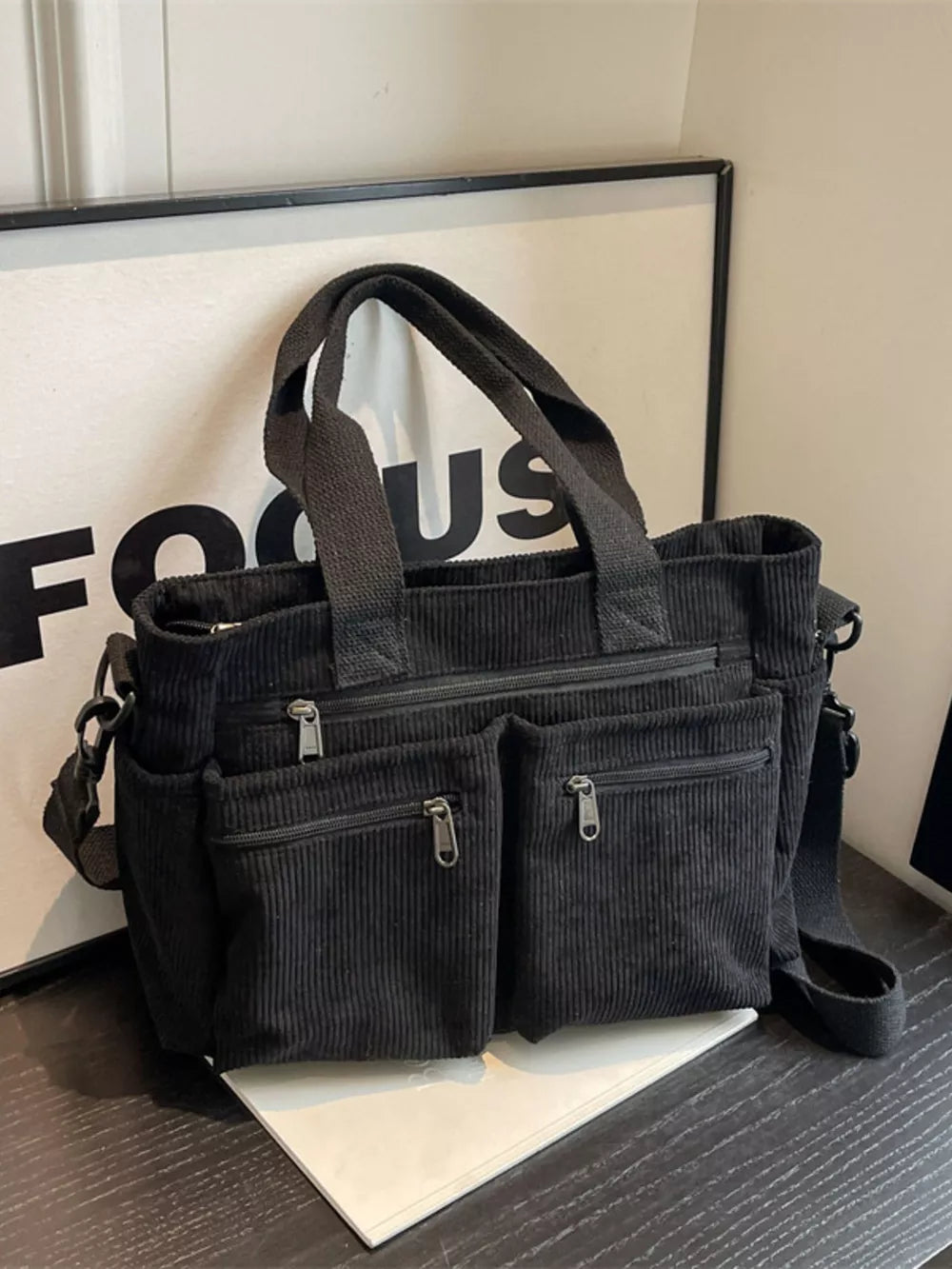 Black corduroy crossbody bag with multiple zippered pockets and top handles.