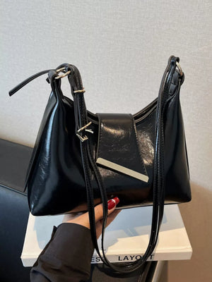 Black patent leather crossbody bag with adjustable strap and silver hardware detail.