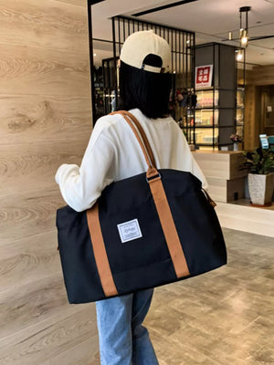 Large black Oxford cloth travel bag with contrast tan straps and white label
