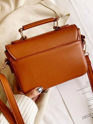Brown leather crossbody bag with top handle and adjustable strap.