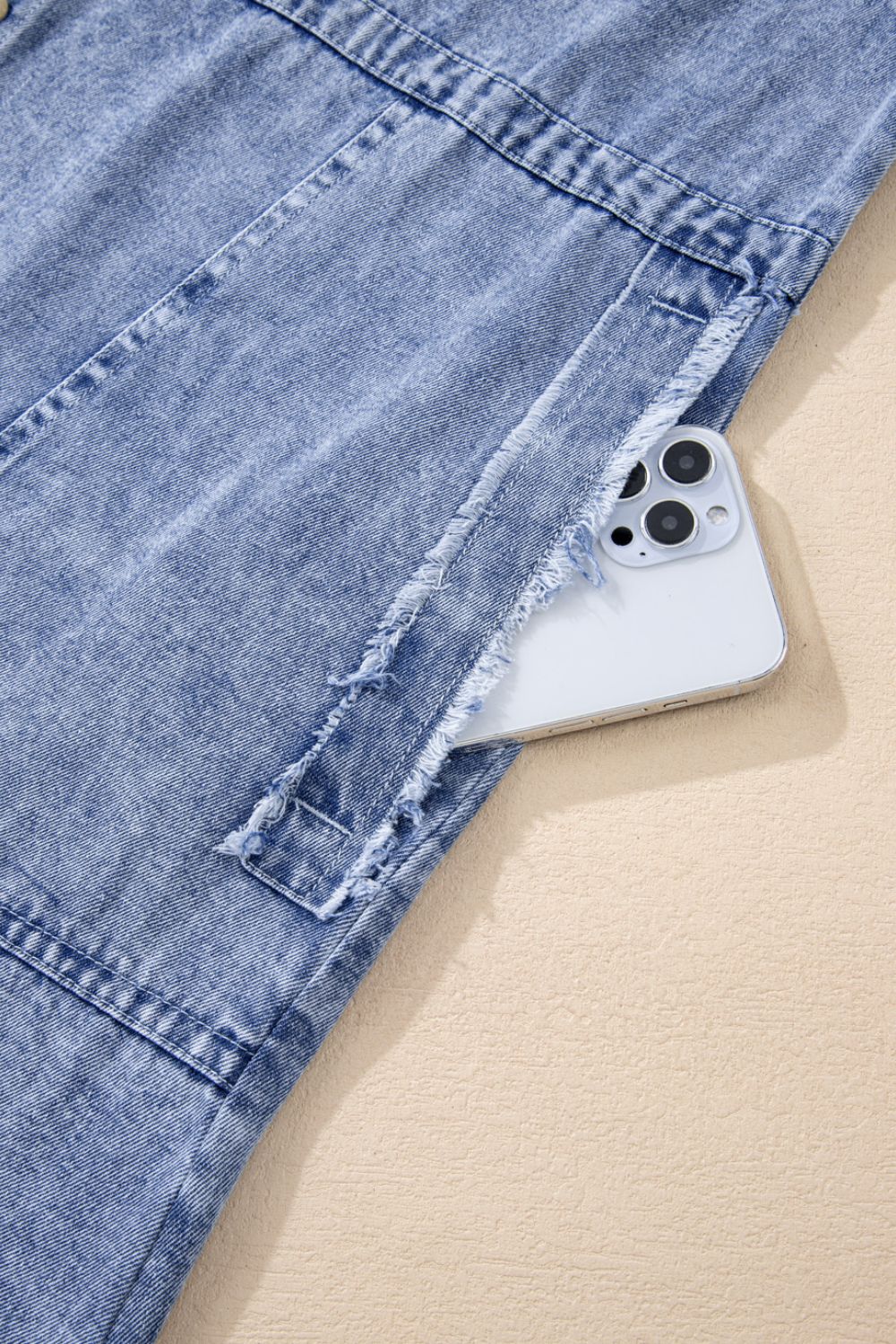 Acid wash denim shirtdress with raw hem detail and pocket holding a phone.