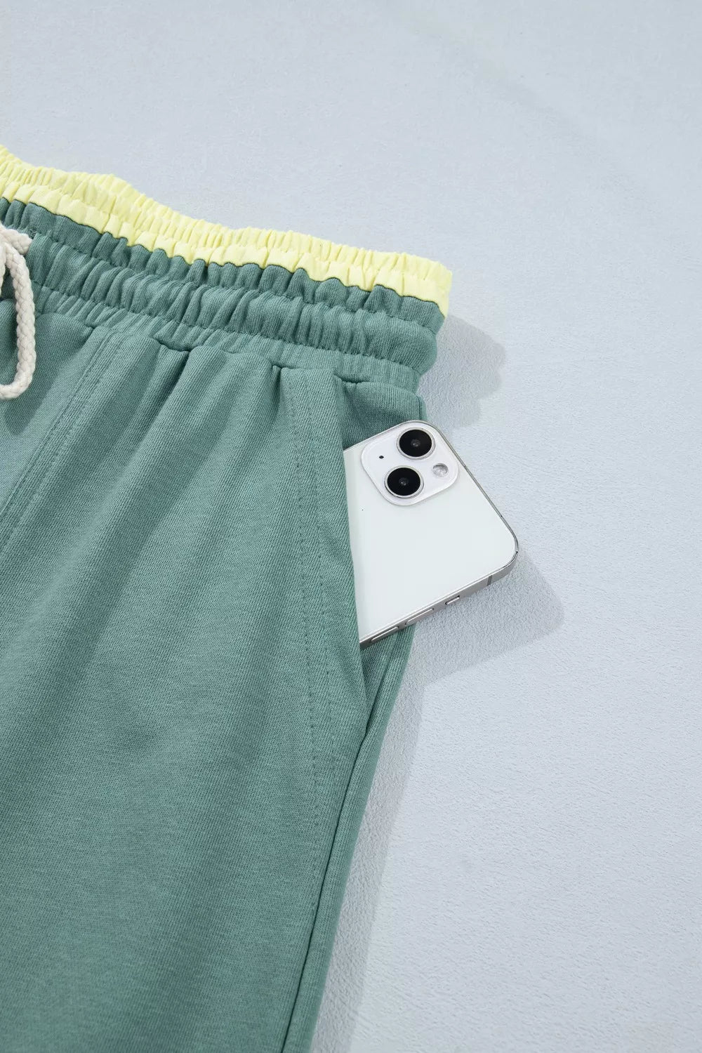 Green cotton sweatpants with yellow waistband and drawstring, phone in pocket.