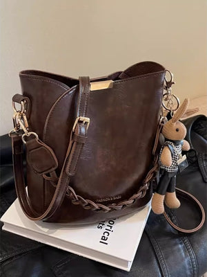 Brown braided bucket crossbody bag with a cute bunny charm.