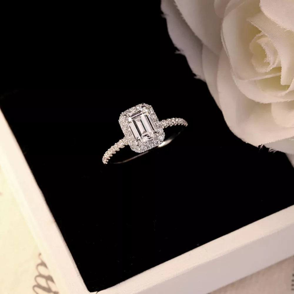 Radiant moissanite engagement ring in silver with emerald-cut center stone and halo accent stones.