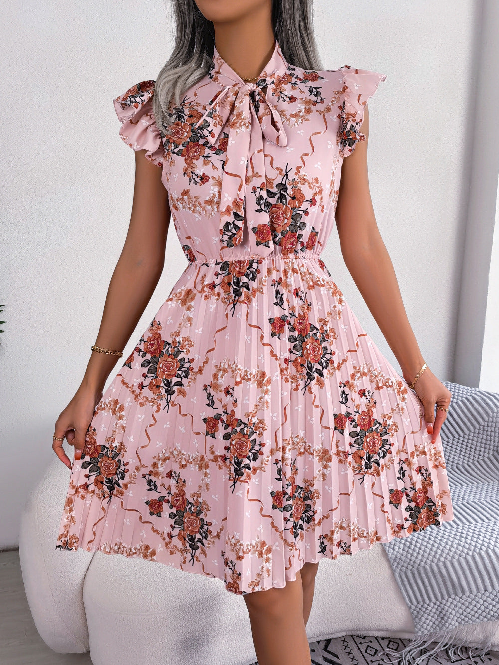 Blush pink floral mini dress with ruffled sleeves, bow neckline, and pleated A-line skirt.