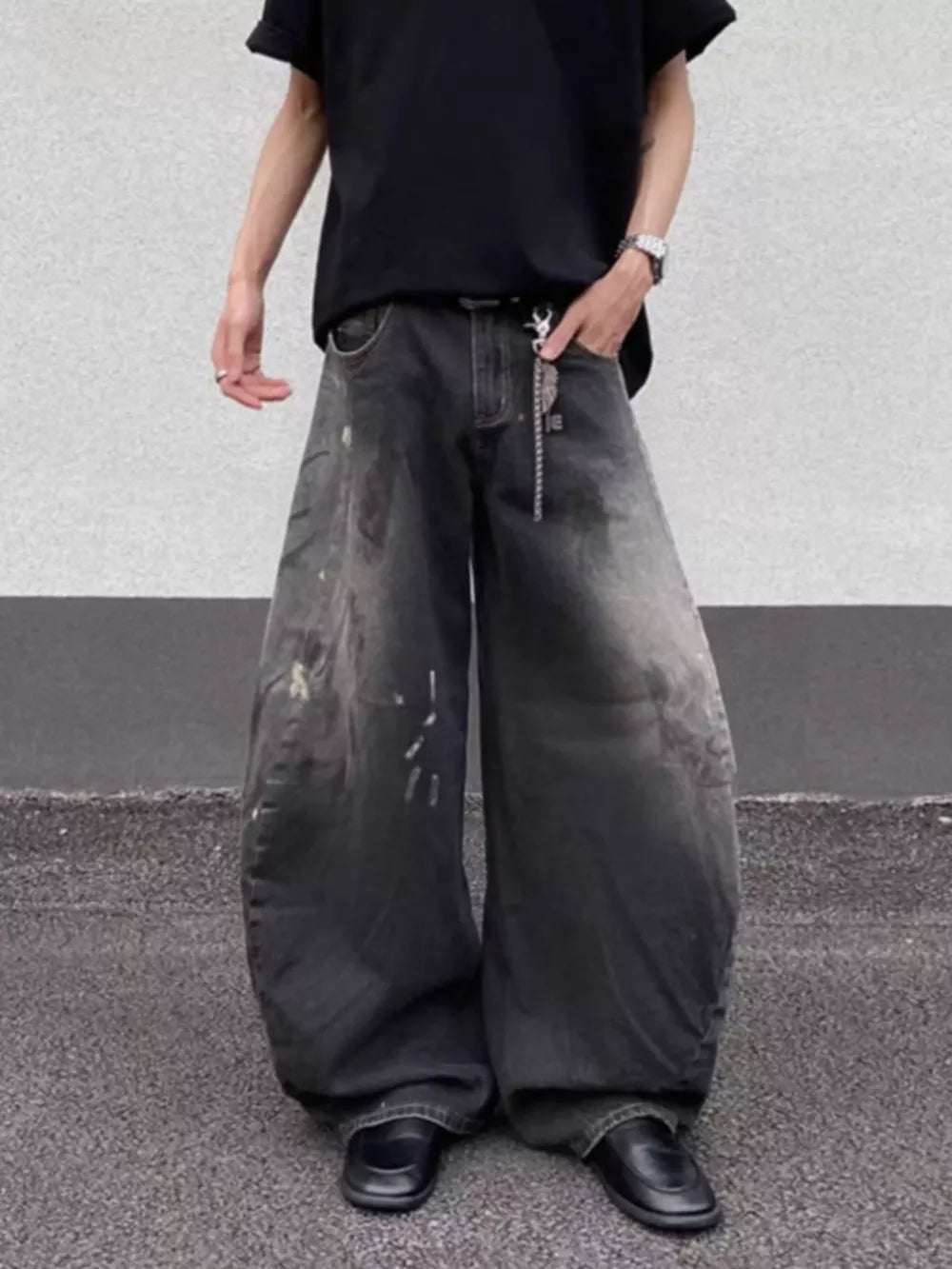Men's wide leg distressed jeans in dark wash denim with paint splatters and a chain detail.