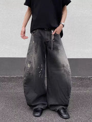 Men's wide leg distressed jeans in dark wash denim with paint splatters and a chain detail.