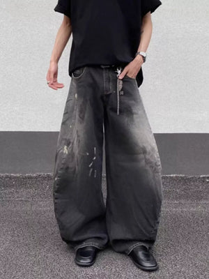 Men's wide leg distressed jeans in dark wash denim with paint splatters and a chain detail.