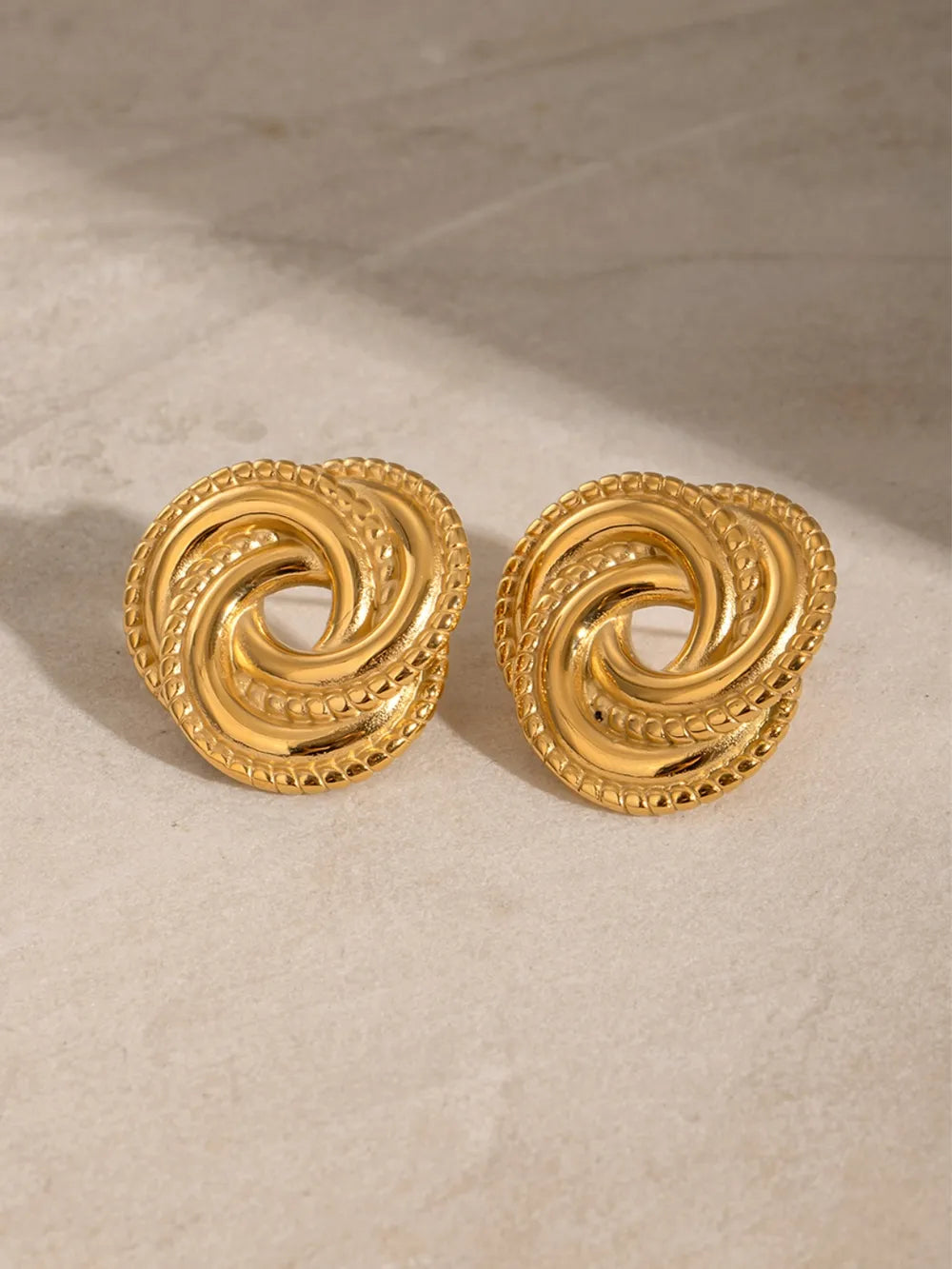 Gold swirl knot stud earrings with textured rope edge detail