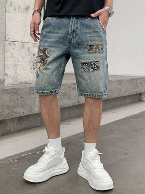 Men's blue denim shorts with graphic patchwork details and distressed accents.