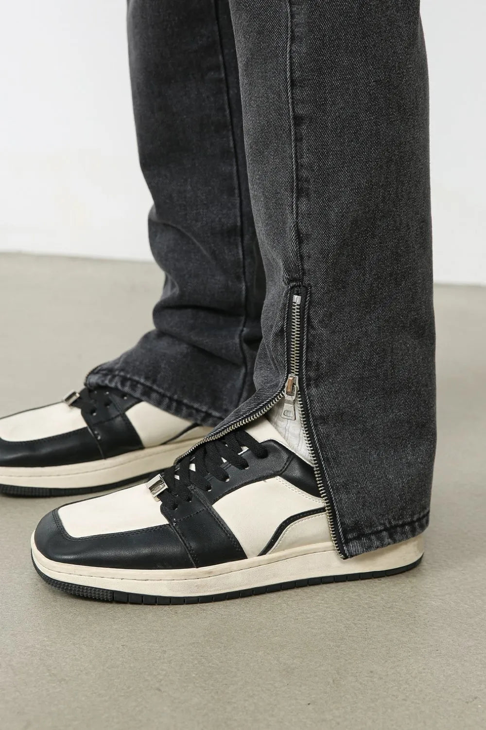 Dark washed denim trousers with a split hem zipper detail shown on the ankle.