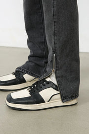 Dark washed denim trousers with a split hem zipper detail shown on the ankle.