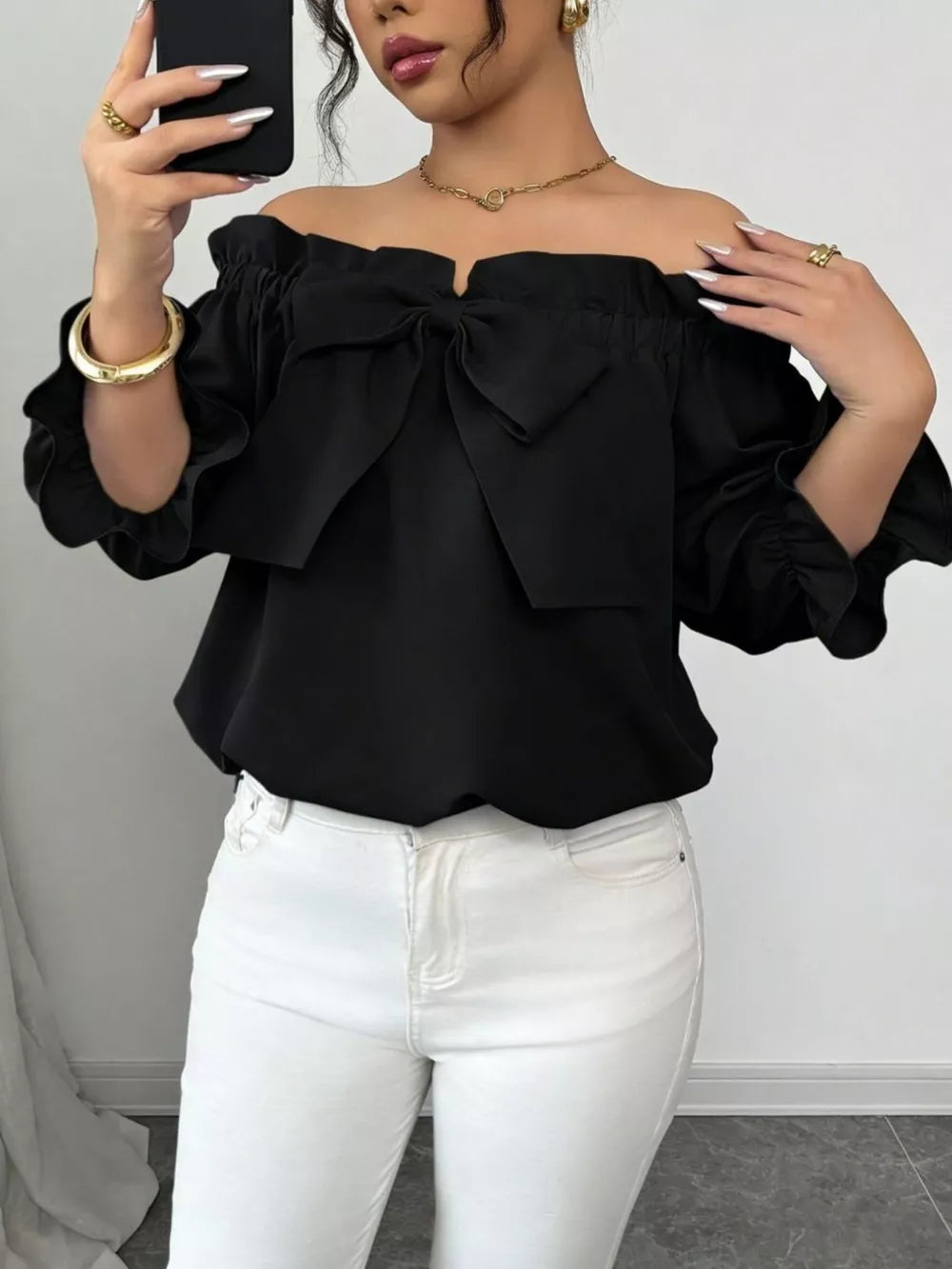 Black off-the-shoulder blouse with ruffled bow detail and puff sleeves.