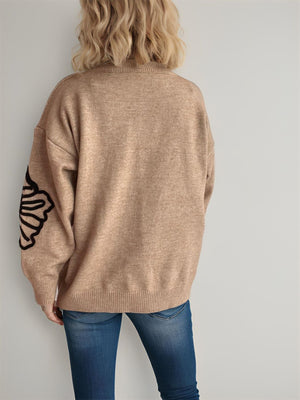 Tan knit sweater with black blossom detail on sleeve.