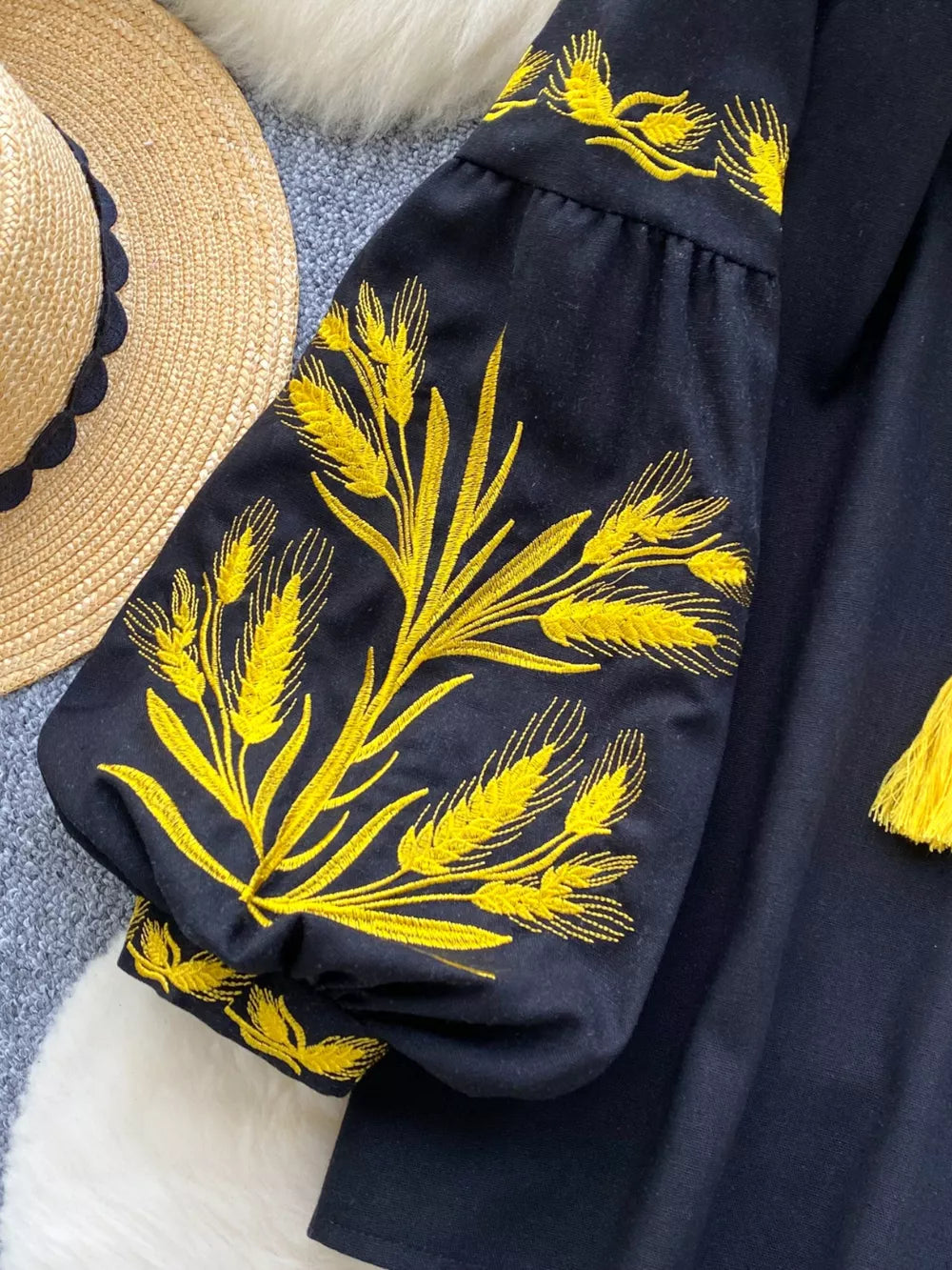 Black tie-neck blouse with yellow wheat embroidery on puff sleeves.