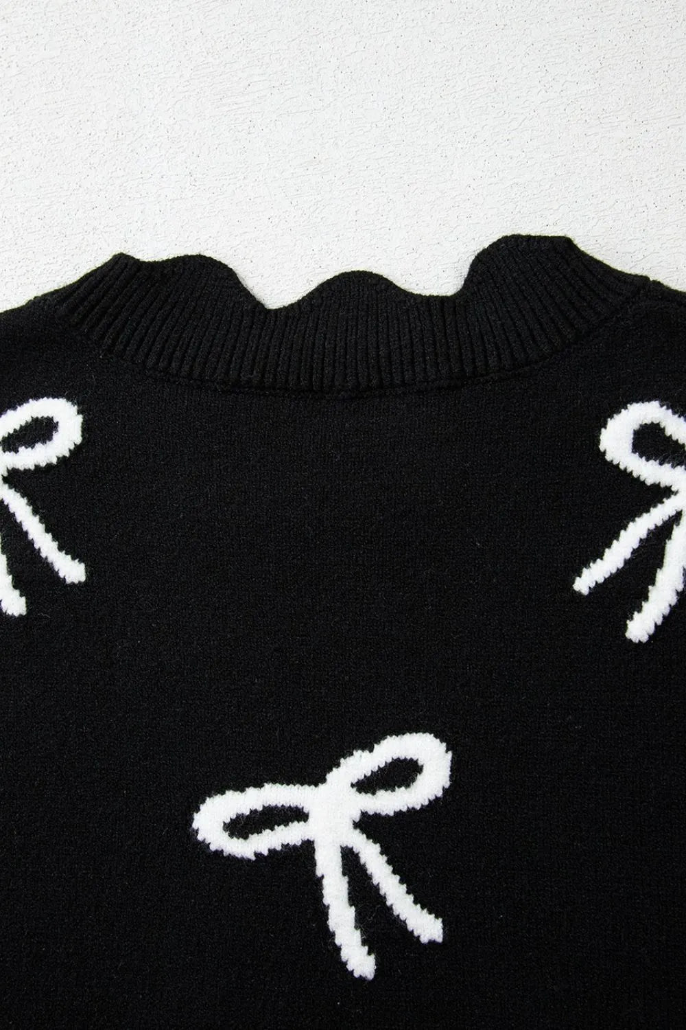 Black knit vest with white bow print and scalloped neckline