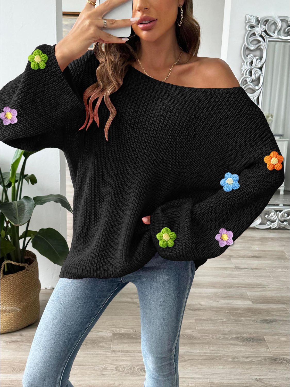 Black knit sweater with colorful embroidered floral appliques on the sleeves.