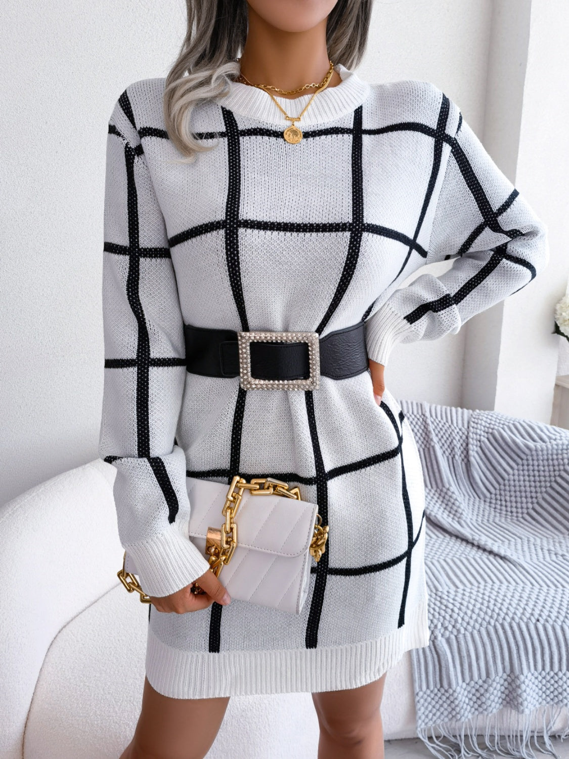 White geometric grid knit mini dress with long sleeves and crew neck, styled with a black belt and white quilted bag.