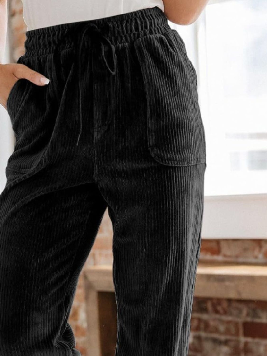 Black corduroy tapered trousers with drawstring waist and pockets.