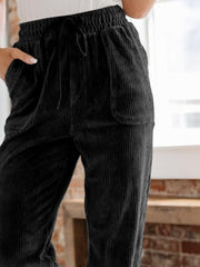 Black corduroy tapered trousers with drawstring waist and pockets.