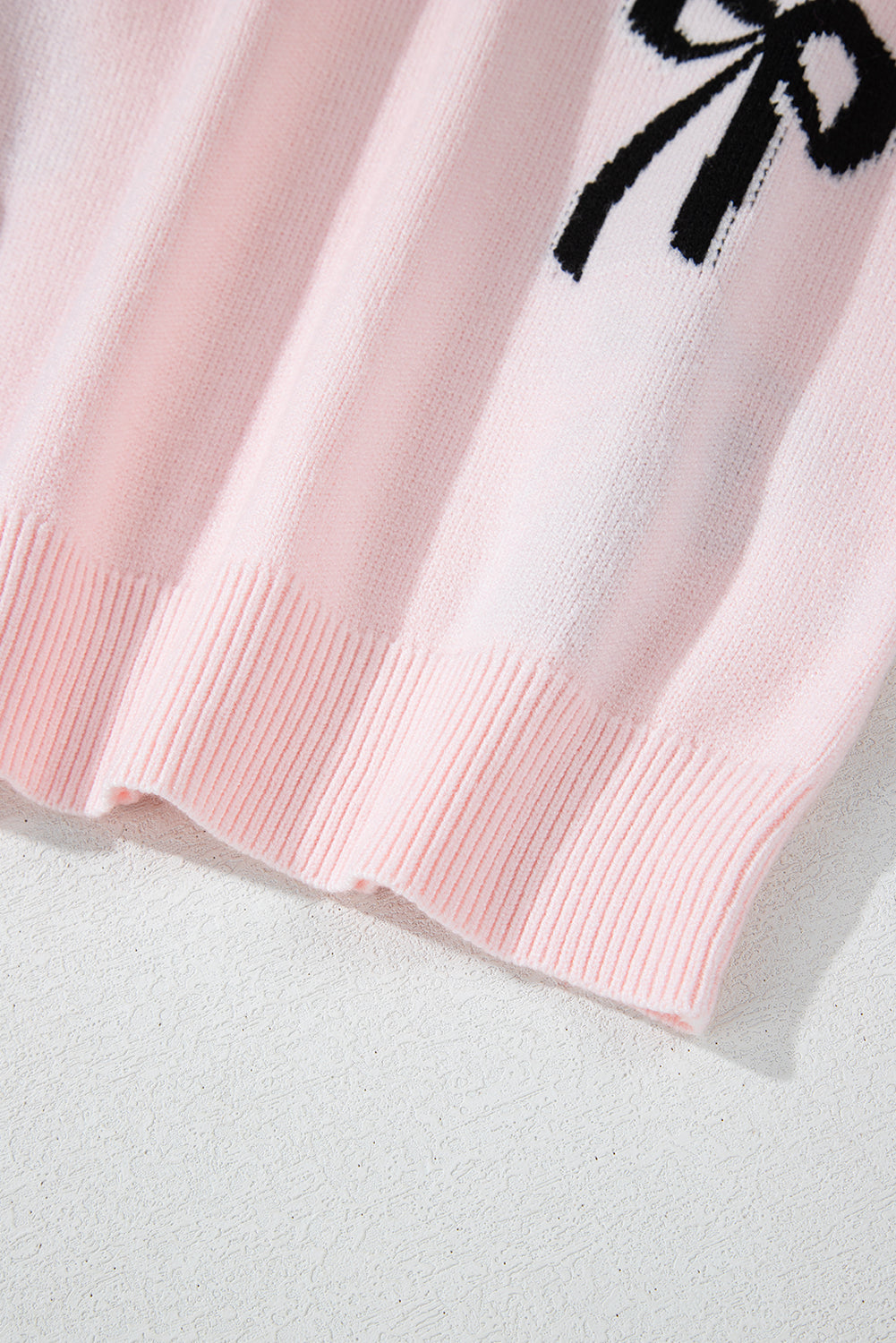 Blush pink knit crewneck sweater with black bow motif detail and ribbed hem.