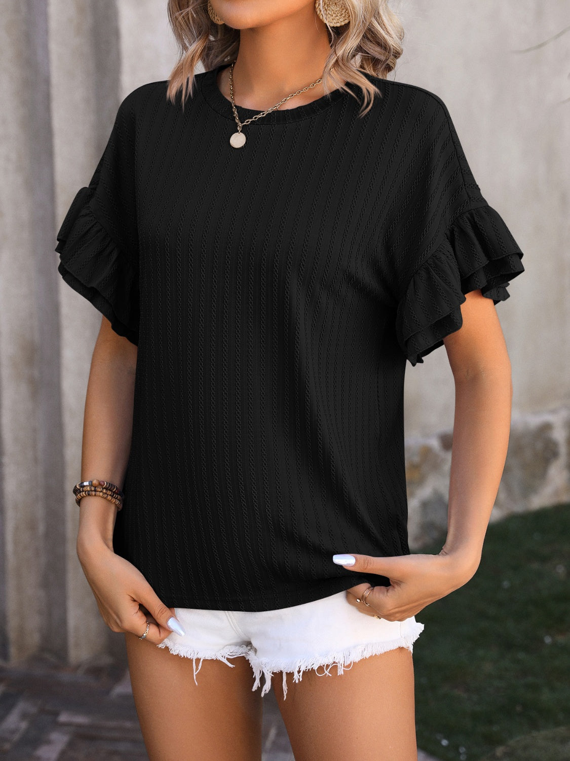Black textured blouse with flutter sleeves and crew neck, styled with white shorts.