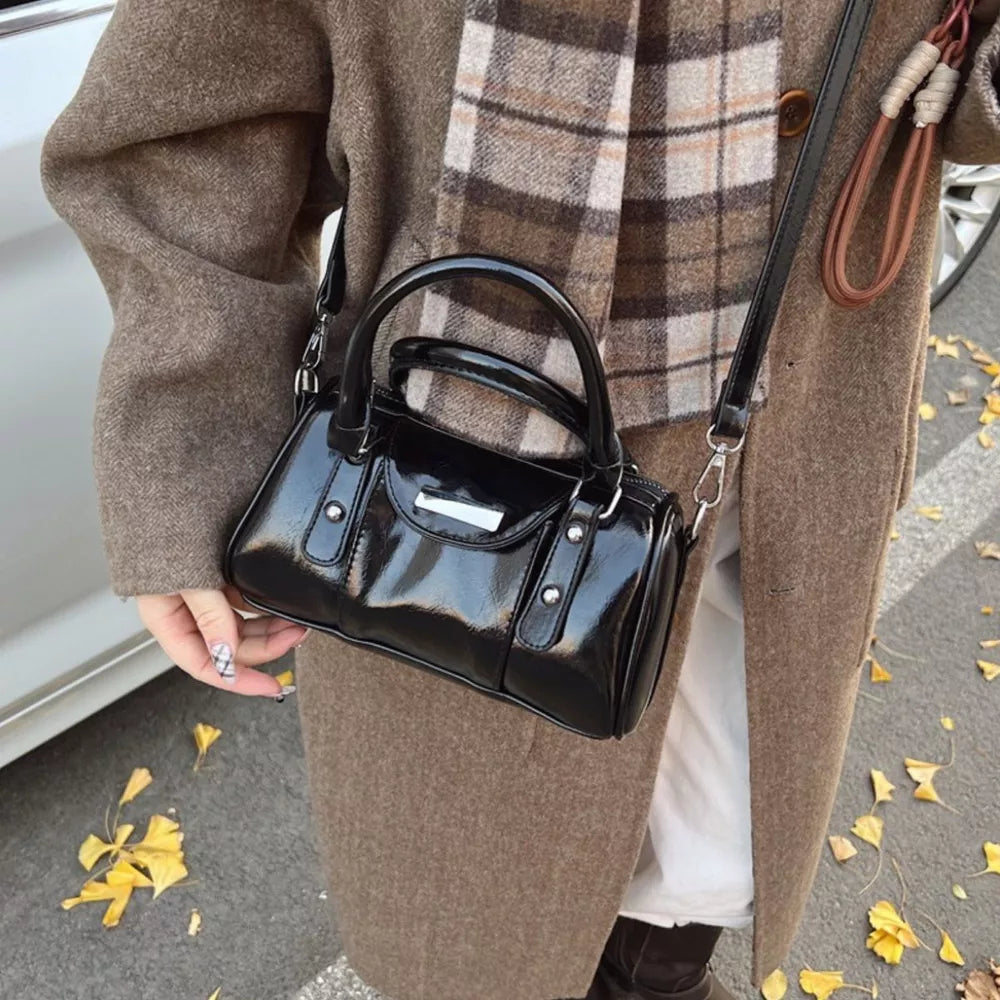 Elegant black patent barrel crossbody bag with top handles and silver hardware.