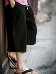 Black relaxed fit cropped sweatpants with drawstring and pockets, worn with sandals.