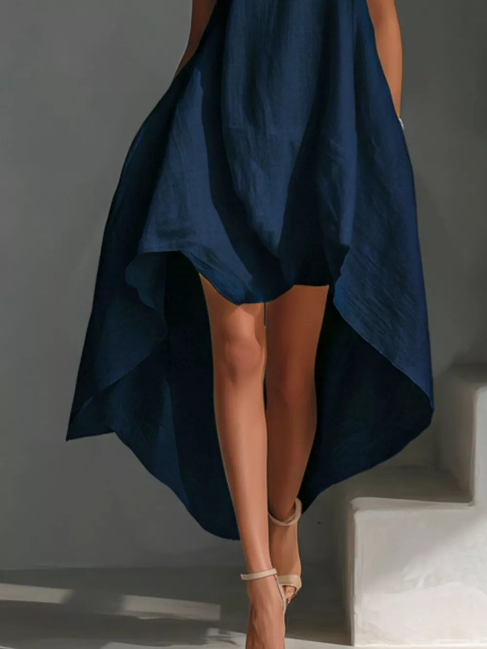 Dark navy asymmetrical sleeveless flowing dress with a high-low hem, styled with sandals.